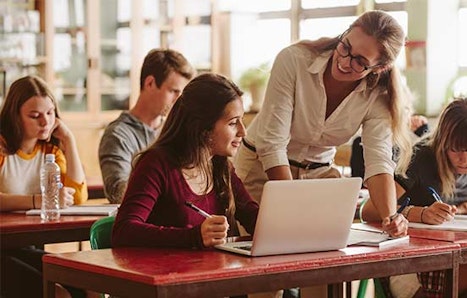 Happy teacher helping students in classroom.