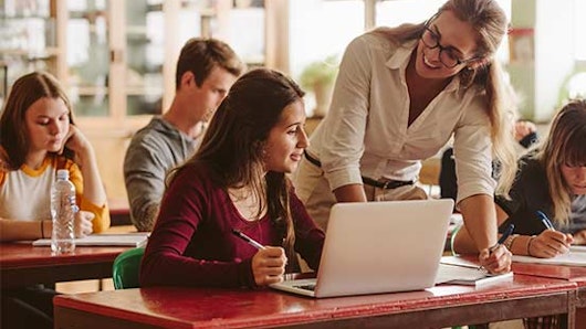 Happy teacher helping students in classroom.