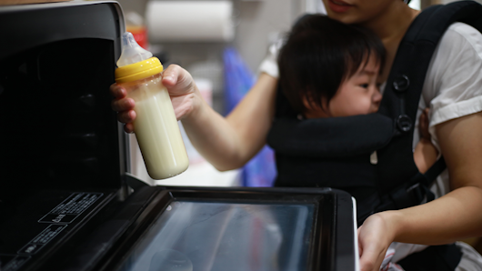 Mother heating up infant milk in microwave.