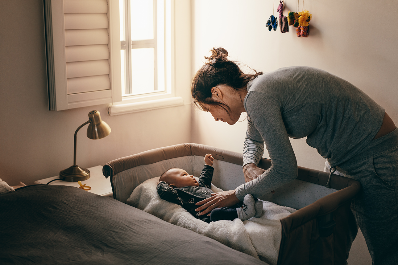 Young mother looking at her baby sleeping in a bassinet.