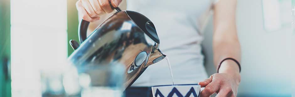 Pouring water from a steel kettle to make a cup of tea.