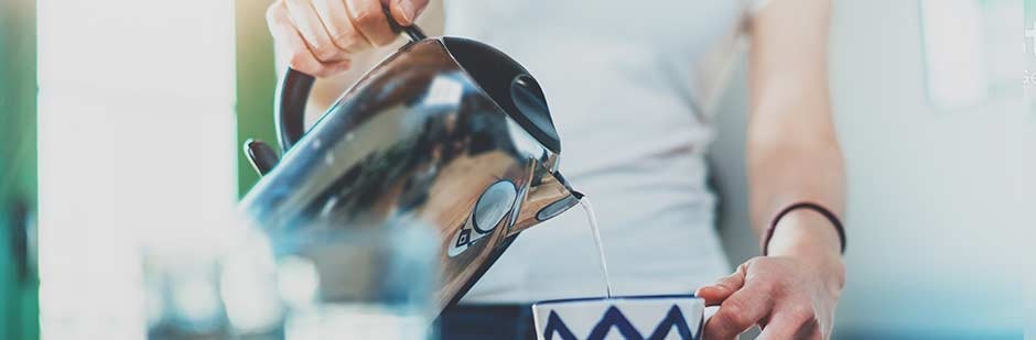 Pouring water from a steel kettle to make a cup of tea.