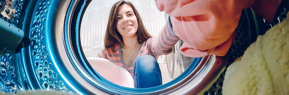 Smiling woman putting clothes in washing machine.