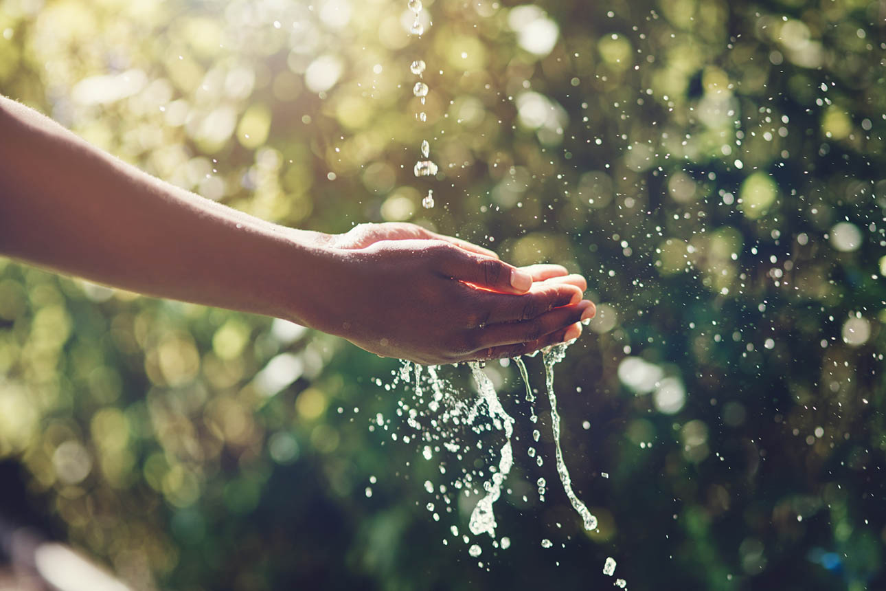 Closeup shot of a man holding his hands under a stream of water outdoors.