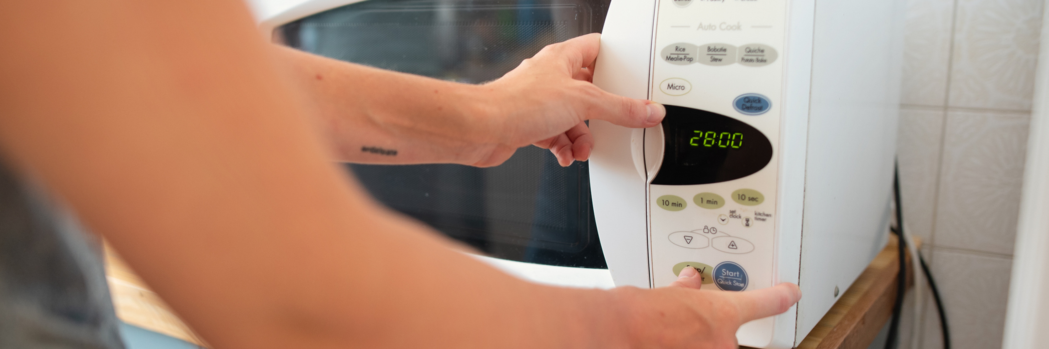 Close-up of a woman warming up food in a microwave while standing at a counter in her kitchen at home.