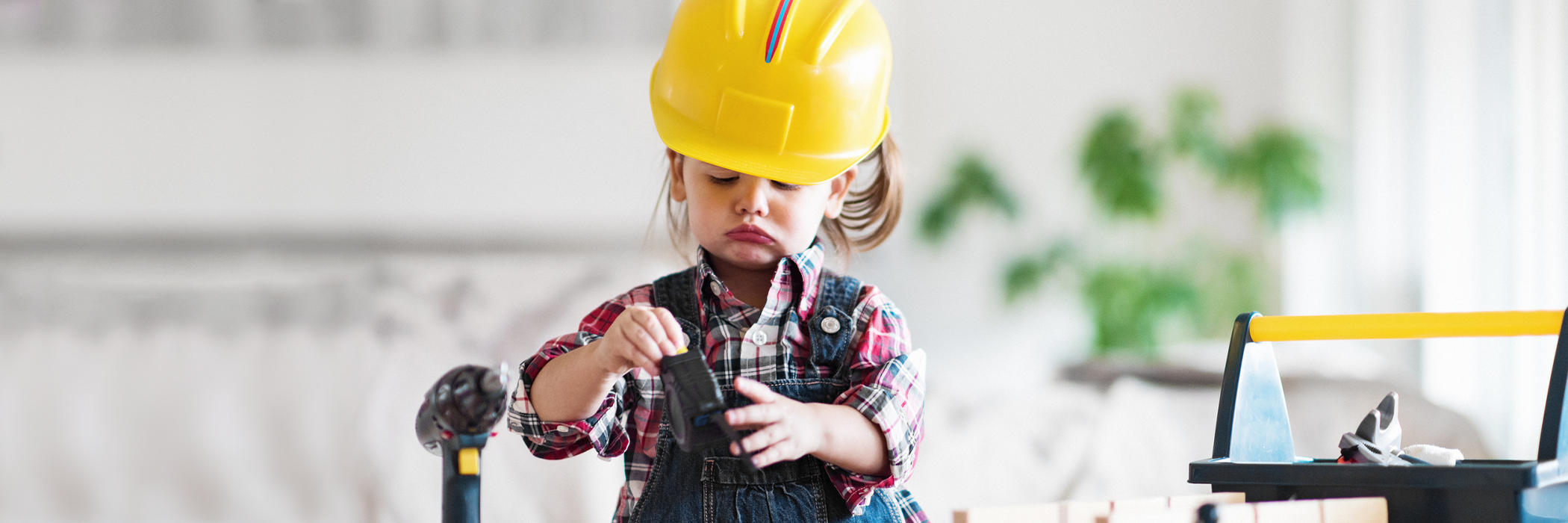 Little 2 year old girl using building hardhat, playing with toy tools.