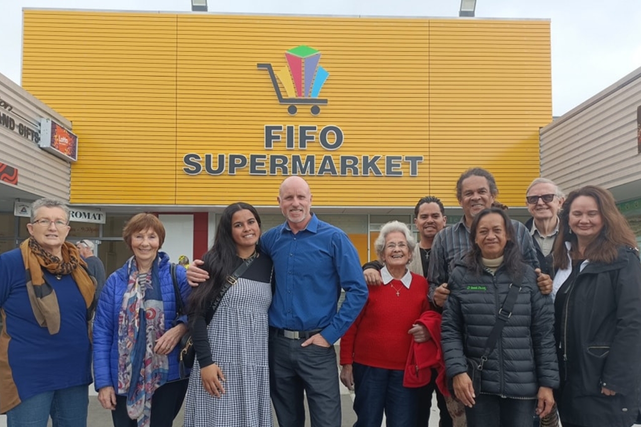 People standing in front of a supermarket sign.