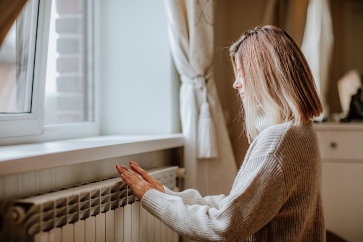Consumer nz website promo image  young blond woman in long winter beige sweater is warming herself near a heater width