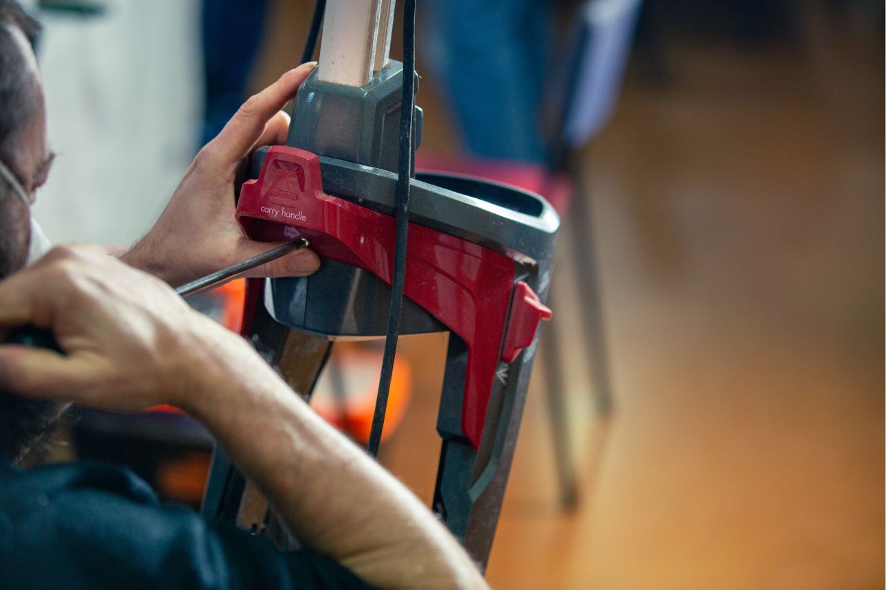 Person using stick vacuum on wooden floor.