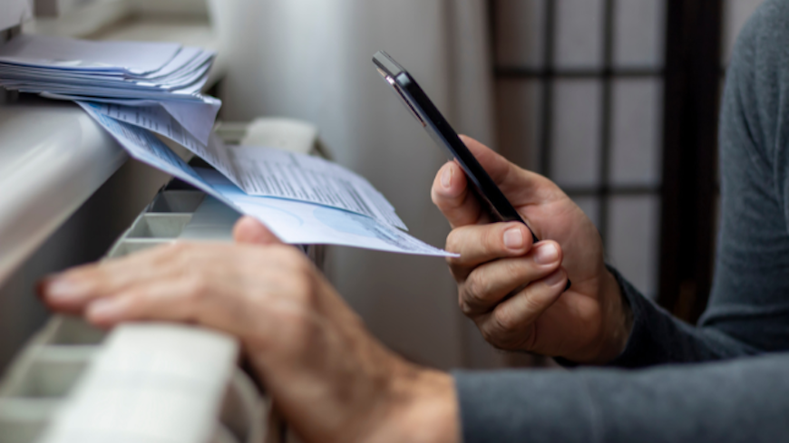 Consumer nz website promo image a renter warms their hands on a heater while reviewing how much their power bill has increased in price width