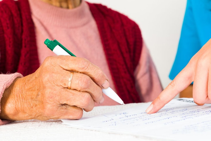 Image of an elderly woman signing papers