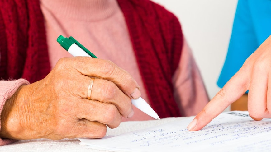 Image of an elderly woman signing papers