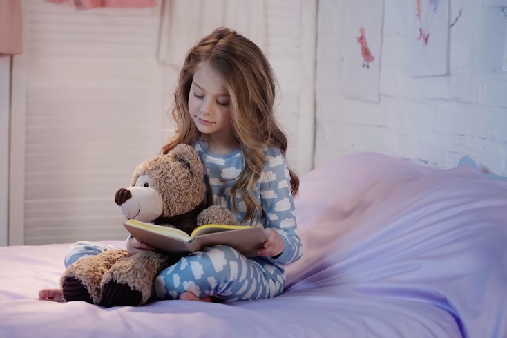 Image of a kid reading a book in bed