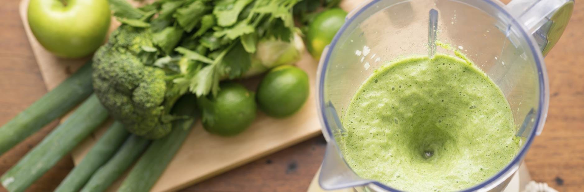 Filled blender beside green fruit and vegetables.