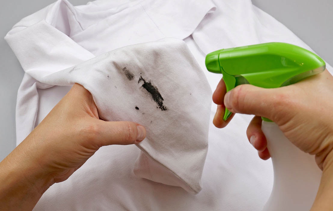 Person spraying spot treatment onto stain on shirt.