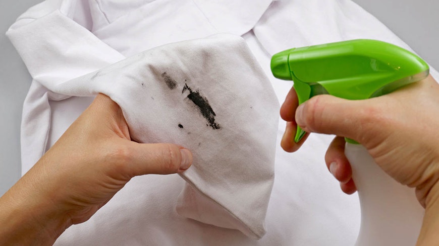 Person spraying spot treatment onto stain on shirt.