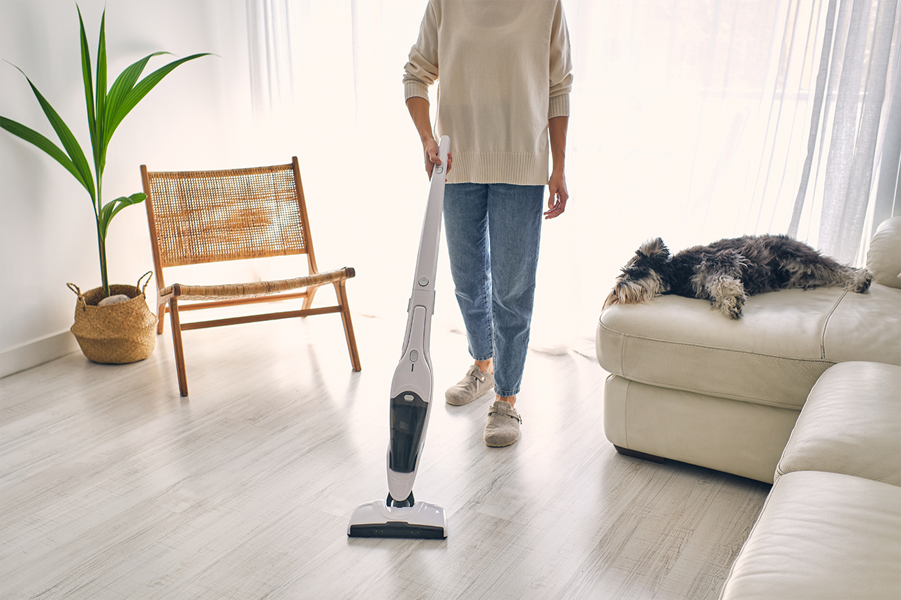 Person using stick vacuum cleaner on hard floor.