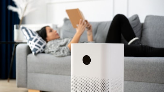 Person using air purifier while reading a book on the couch