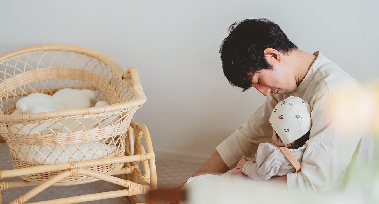 Dad holding baby next to a moses basket.