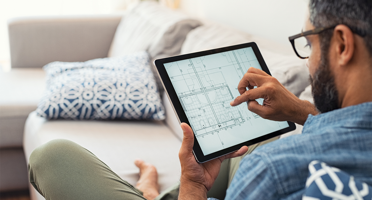 Man hand working with tablet and blueprint on architectural project at home while relaxing on couch.
