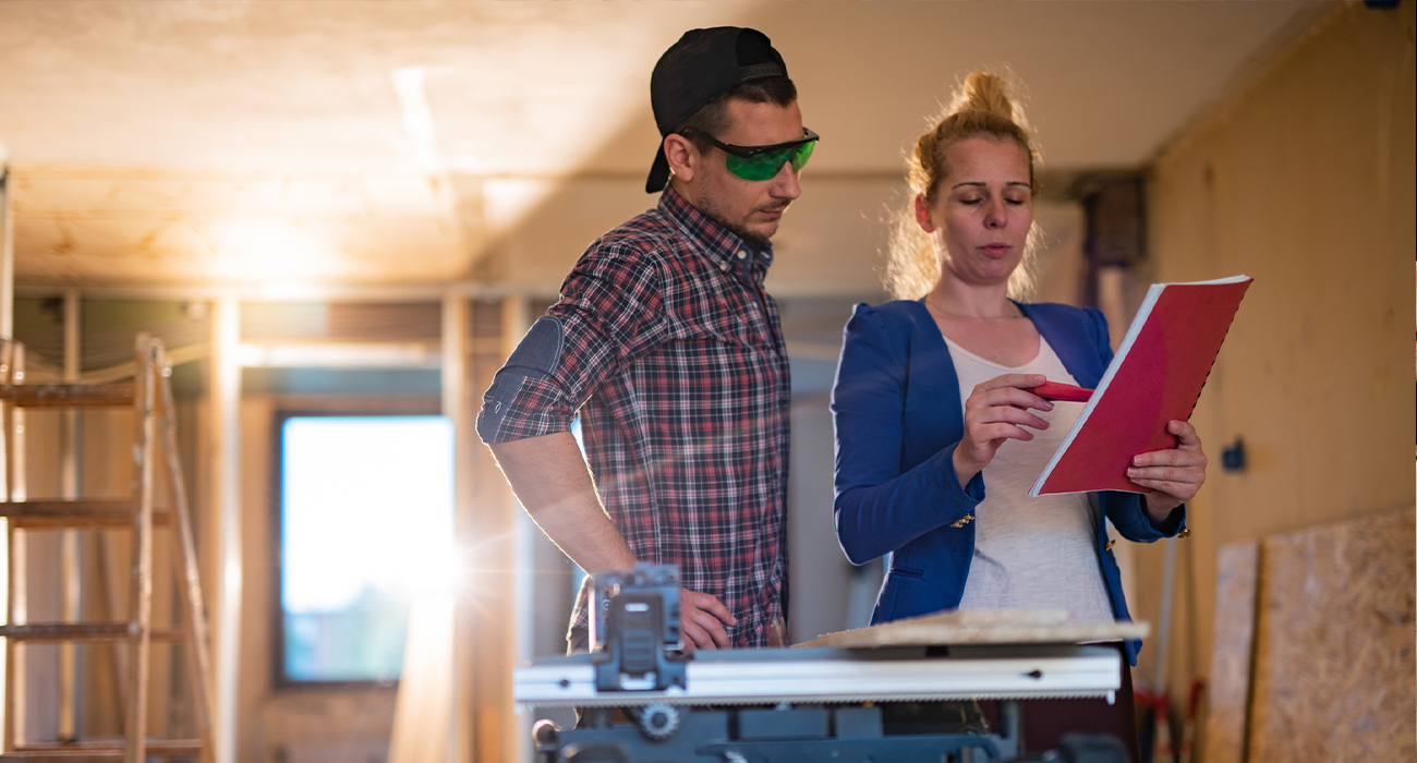 Female building contractor giving instructions to worker on construction site.