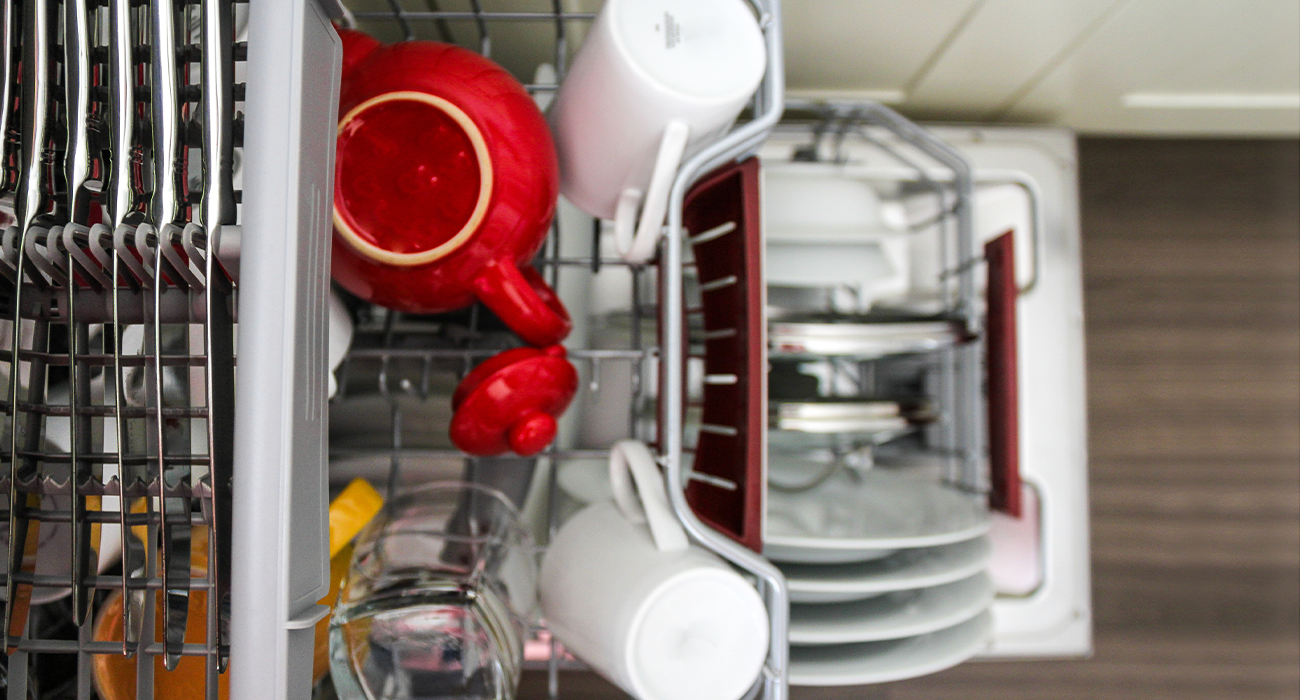 Image depicting a stack of clean plates, mugs and cutlery in a modern dishwasher in a domestic kitchen at home.