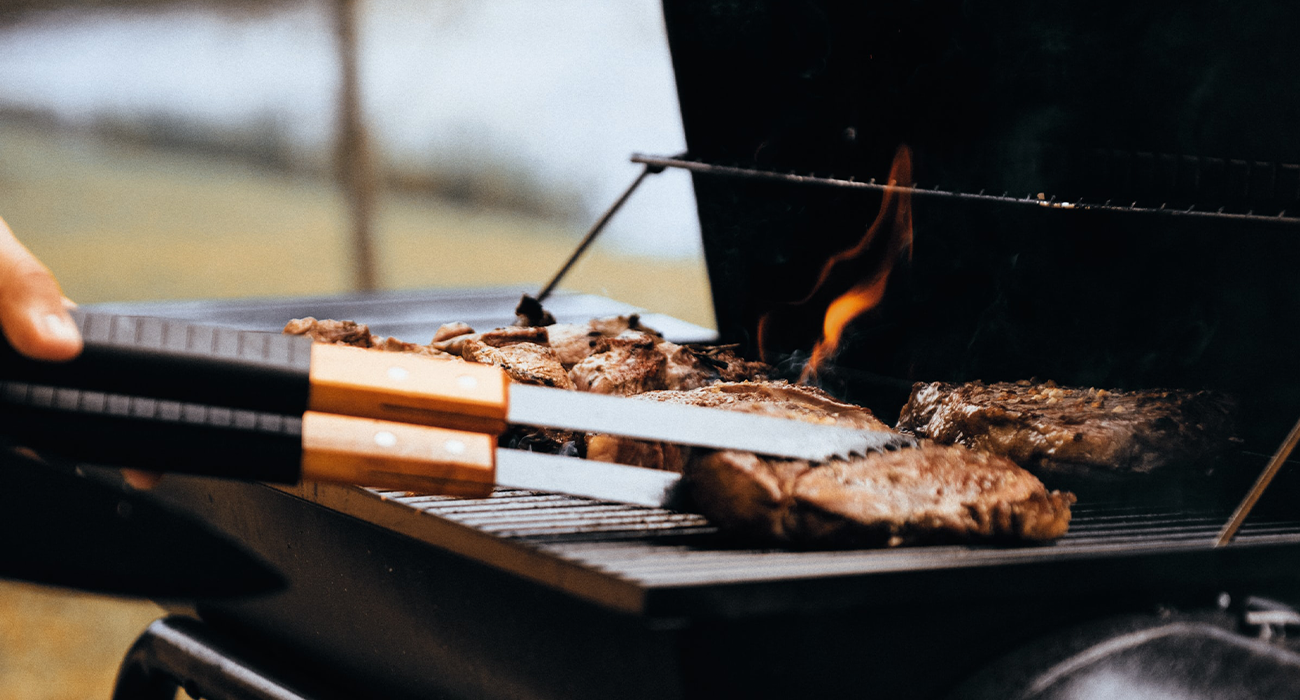 Close-up of person flipping meat on barbecue.