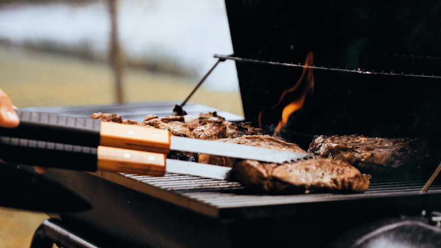 Close-up of person flipping meat on barbecue.