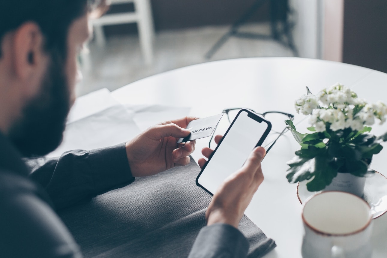 Man looking at phone holding a payment card.