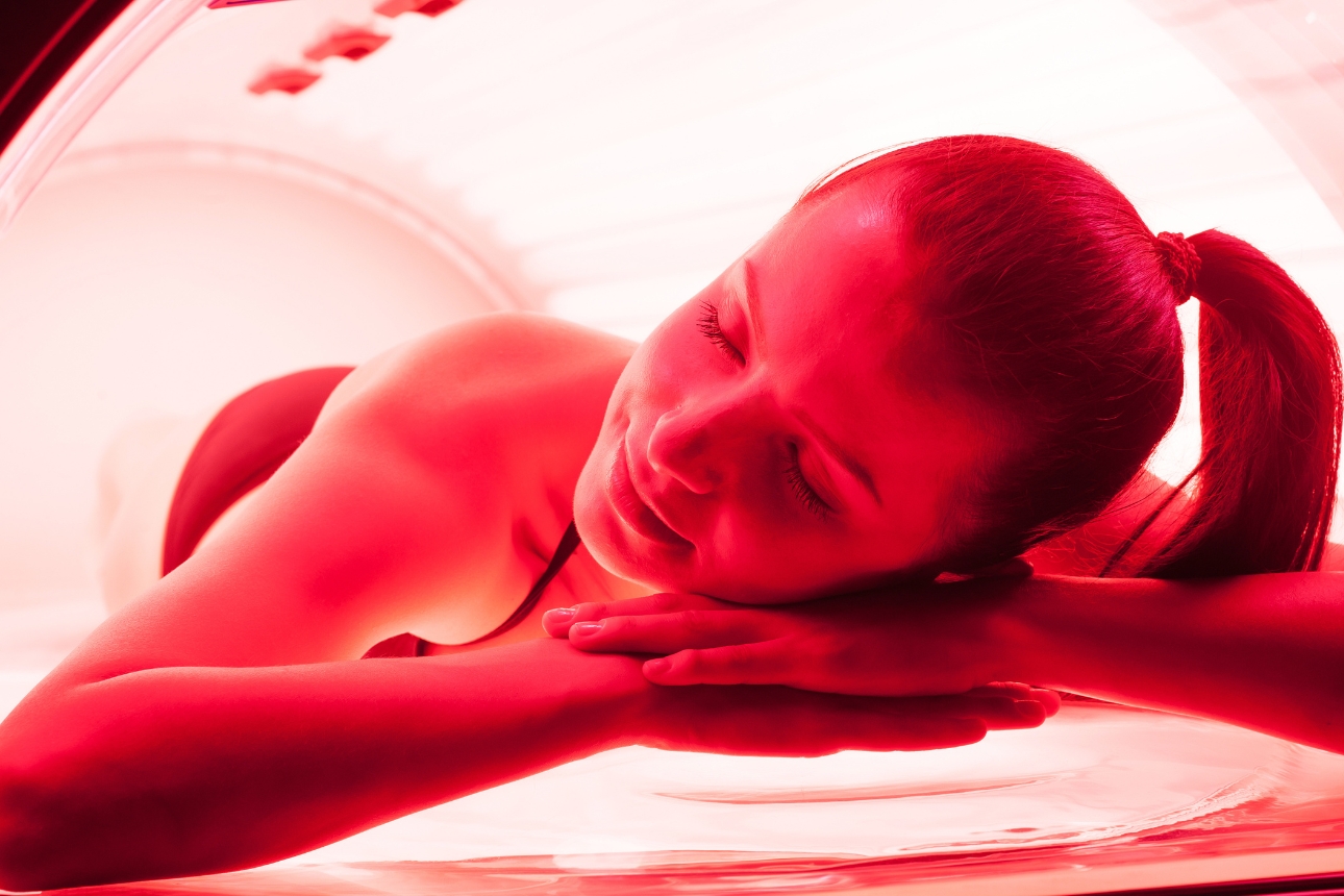 Woman laying in a red light therapy bed.