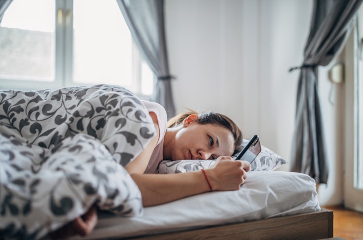 Woman laying in bed using smartphone.