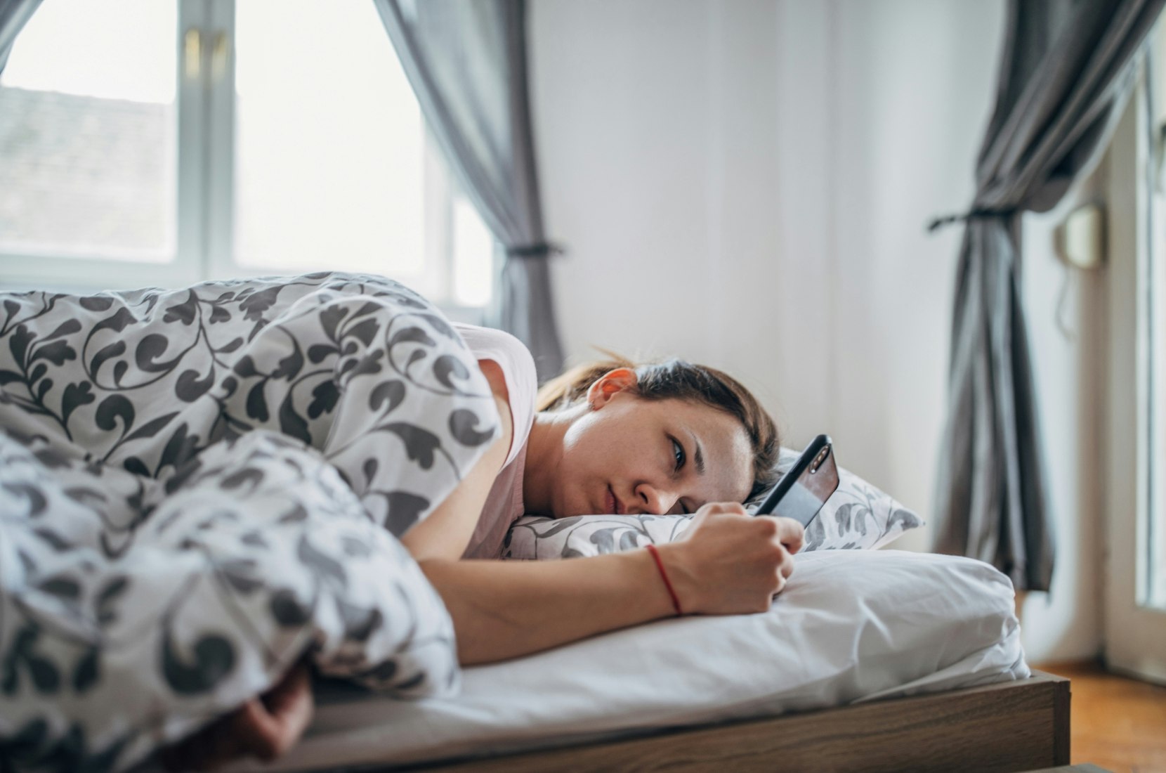 Woman laying in bed using smartphone.